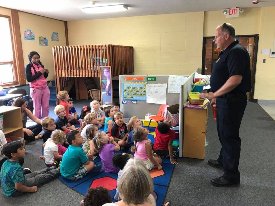 Adult speaking to a group of children sitting on the floor in a classroom