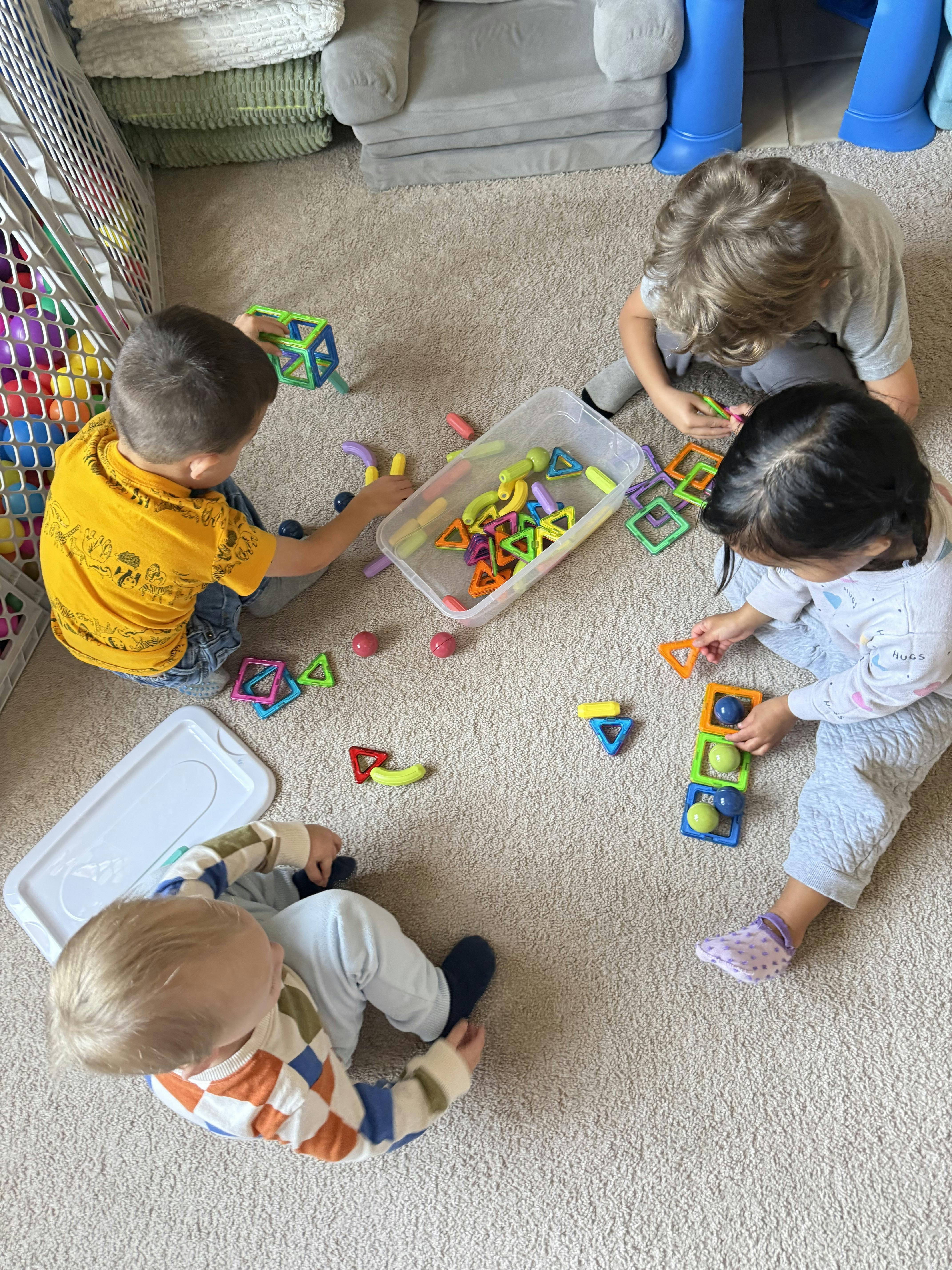 Four children playing with colorful magnetic toys on a carpeted floor