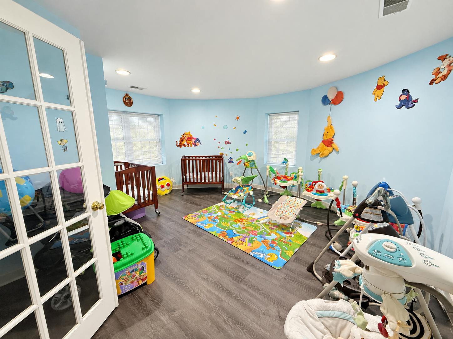 Childcare room with play mats, multiple baby swings, and cribs