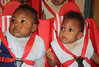 Two babies in red high chairs with safety harnesses