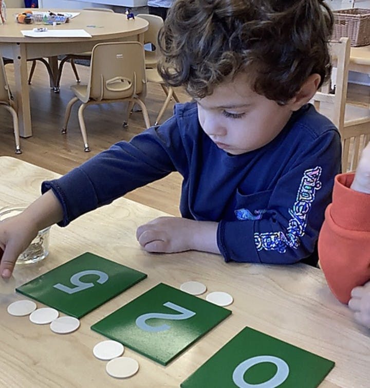 Child playing with number cards and small white circles in a classroom