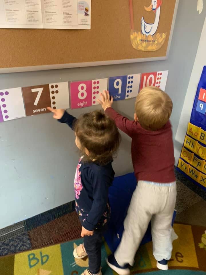 Two children interacting with number cards on a wall