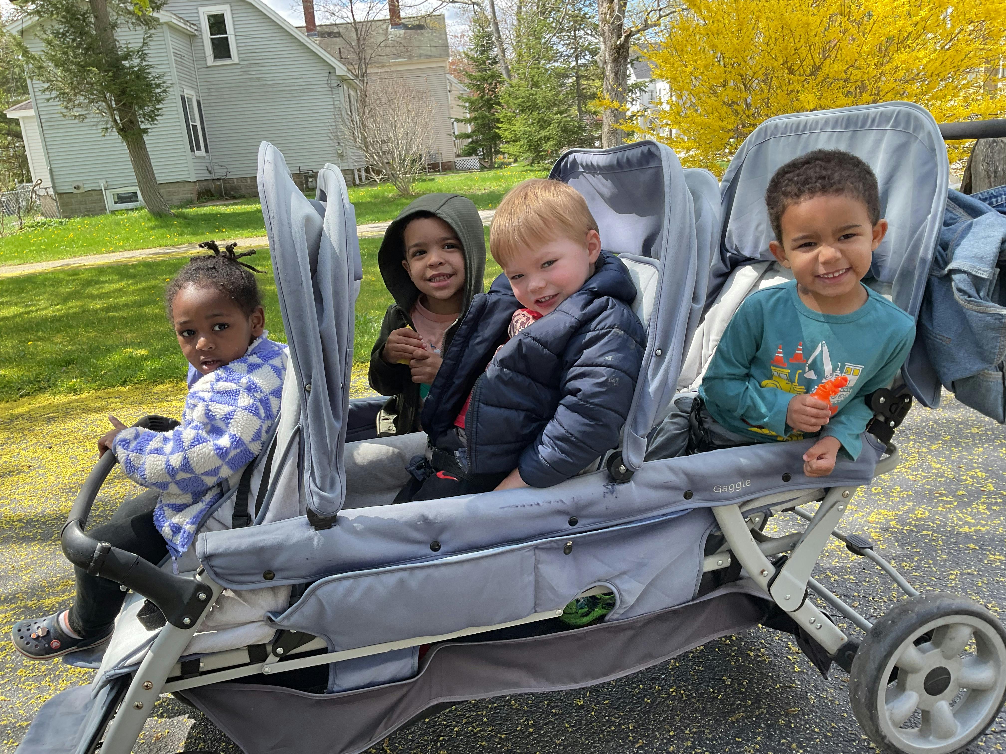 Four children sitting in a large multi-seat stroller outdoors