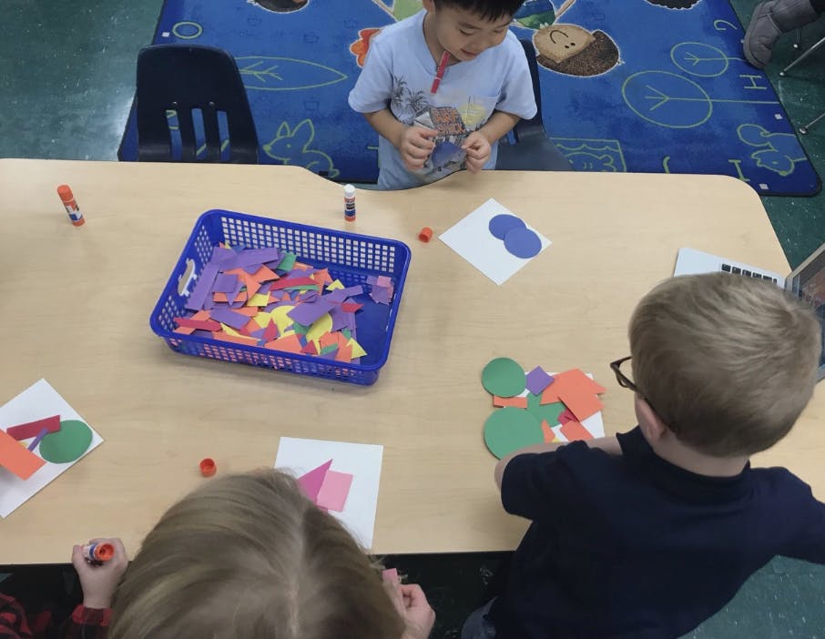 Children at a table doing crafts with colorful paper shapes