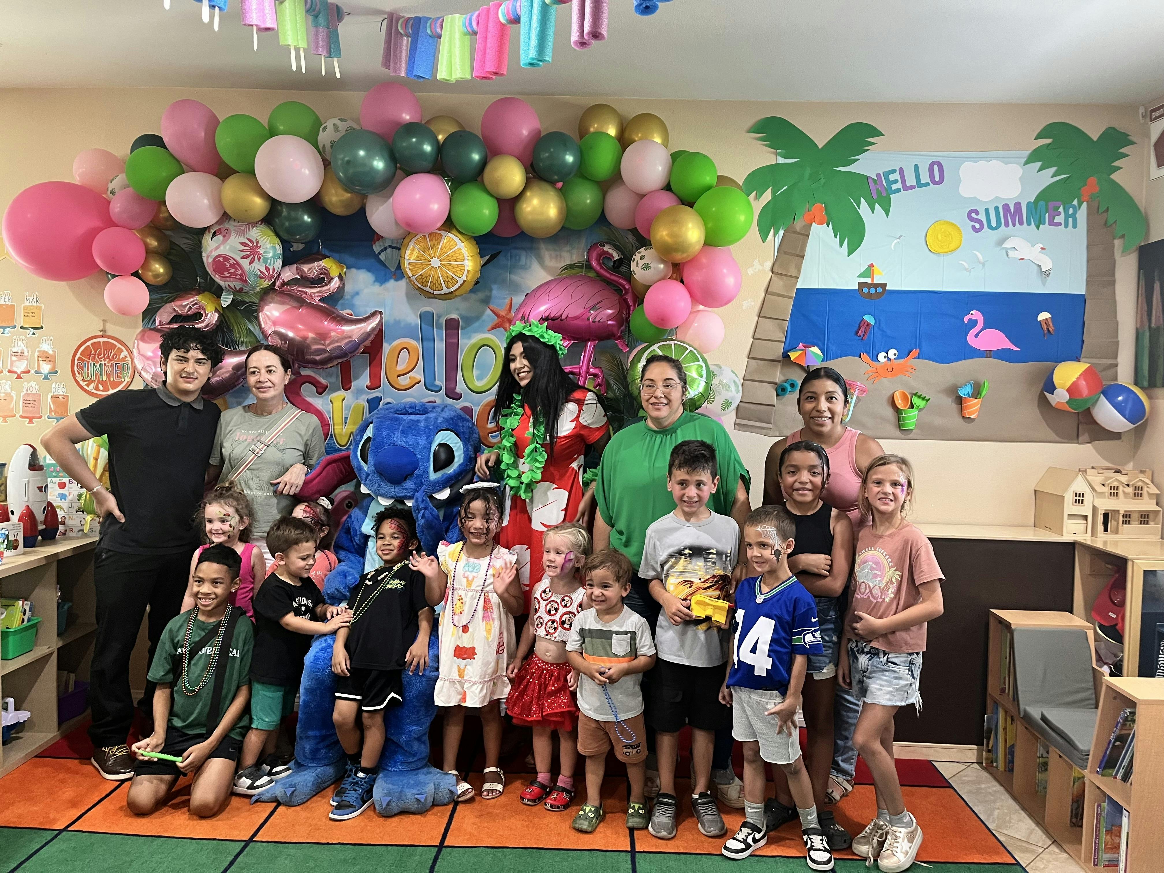 Group of adults and children posing in front of balloons and a summer-themed backdrop