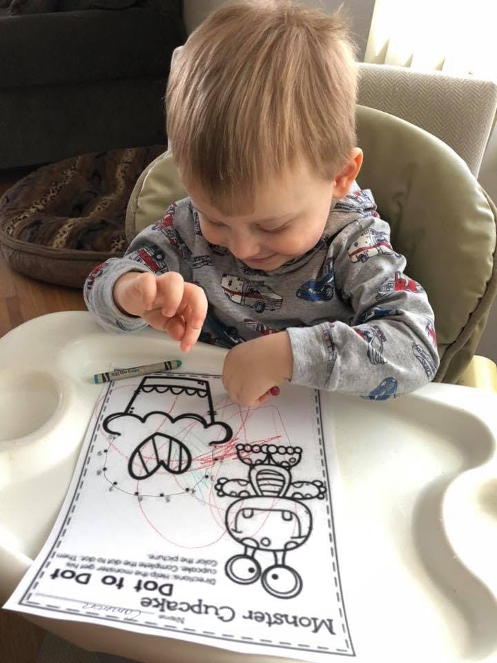 Child in a high chair connecting dots on a Monster Cupcake Dot to Dot worksheet