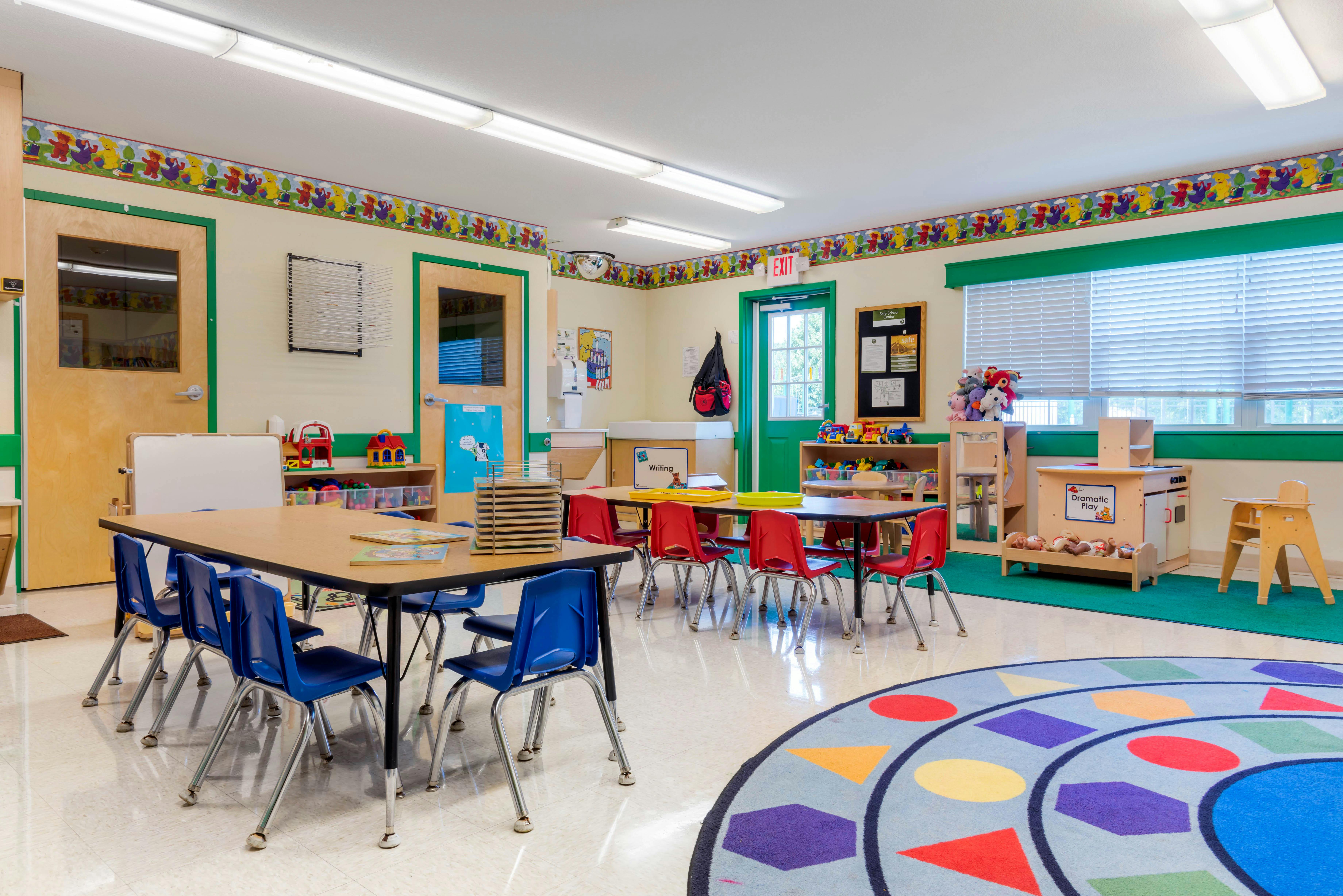 Classroom with child-sized tables and chairs, a play kitchen, and a rug with shapes