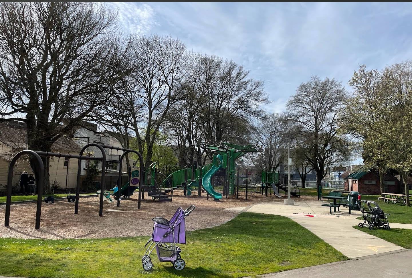 Empty playground with swings, slides, and a purple stroller on the grass