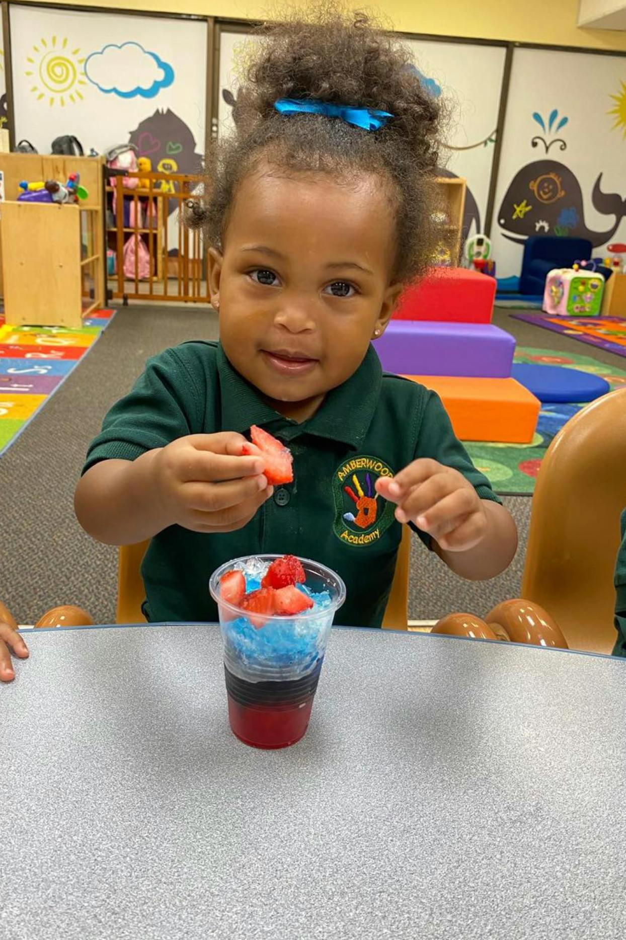 A child in a classroom holding a strawberry over a cup of shaved ice