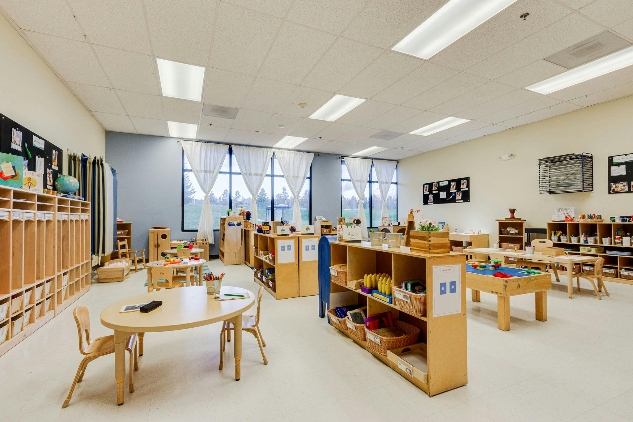 Empty classroom with small tables, chairs, and storage shelves
