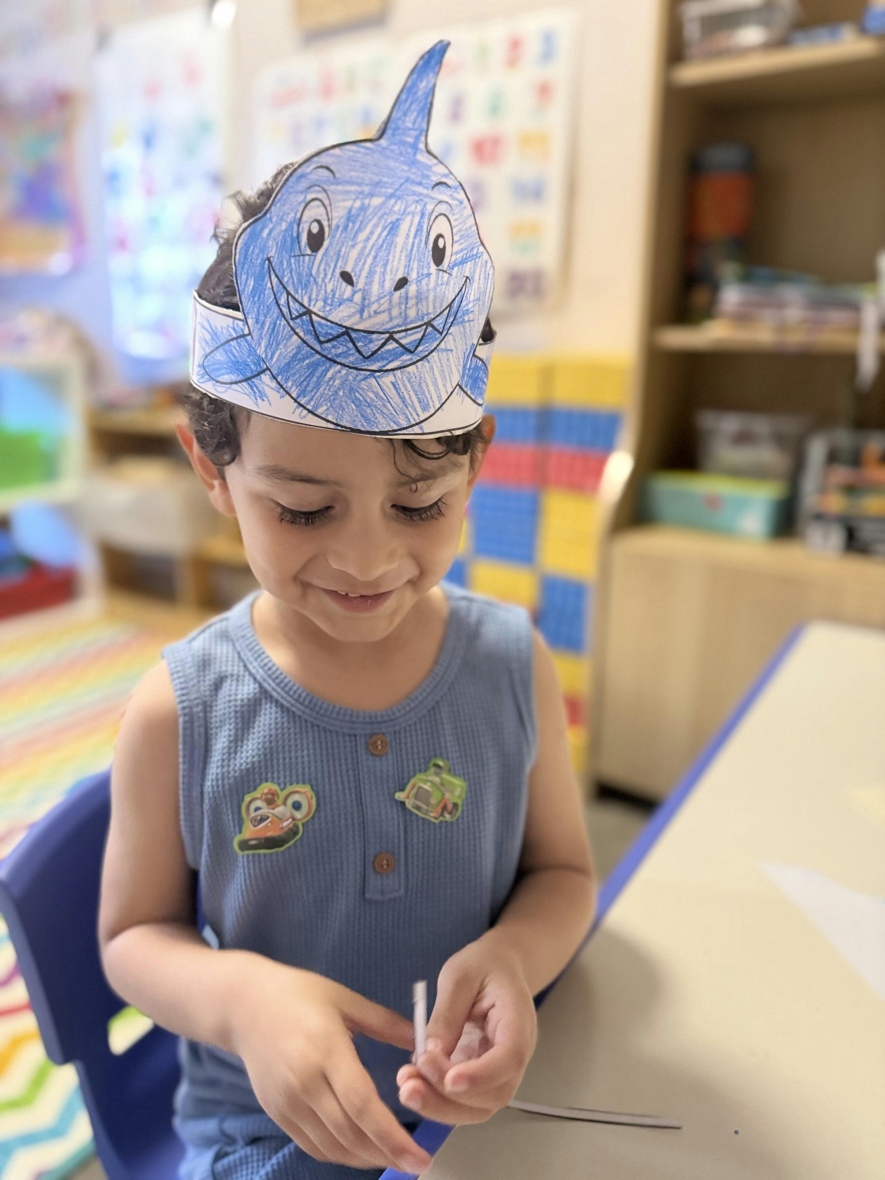 Child wearing a blue shark paper hat, looking down