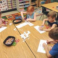 Children cutting paper at a table in a classroom
