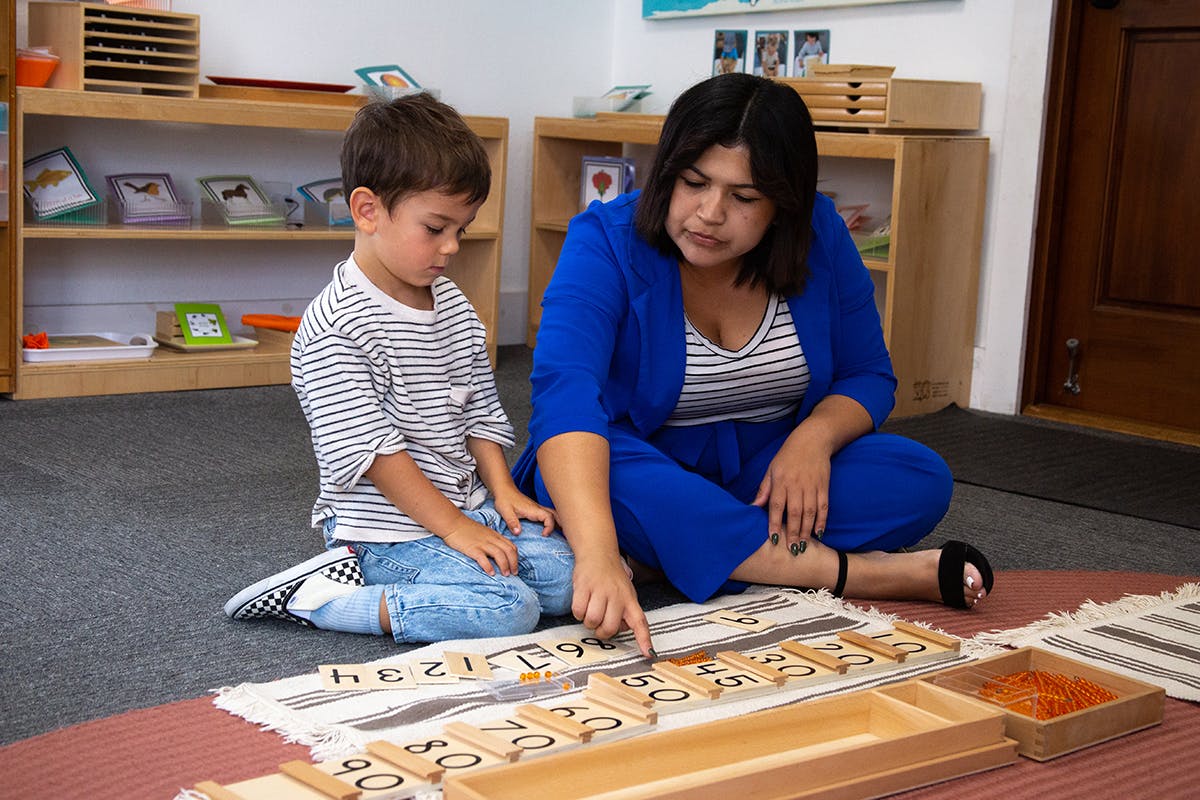 Person and child on floor pointing at wooden letter tiles