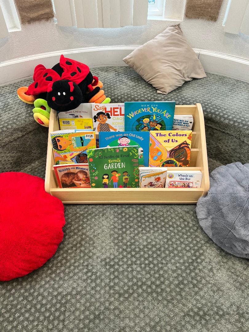 Children's books in a wooden display shelf with a ladybug plush toy