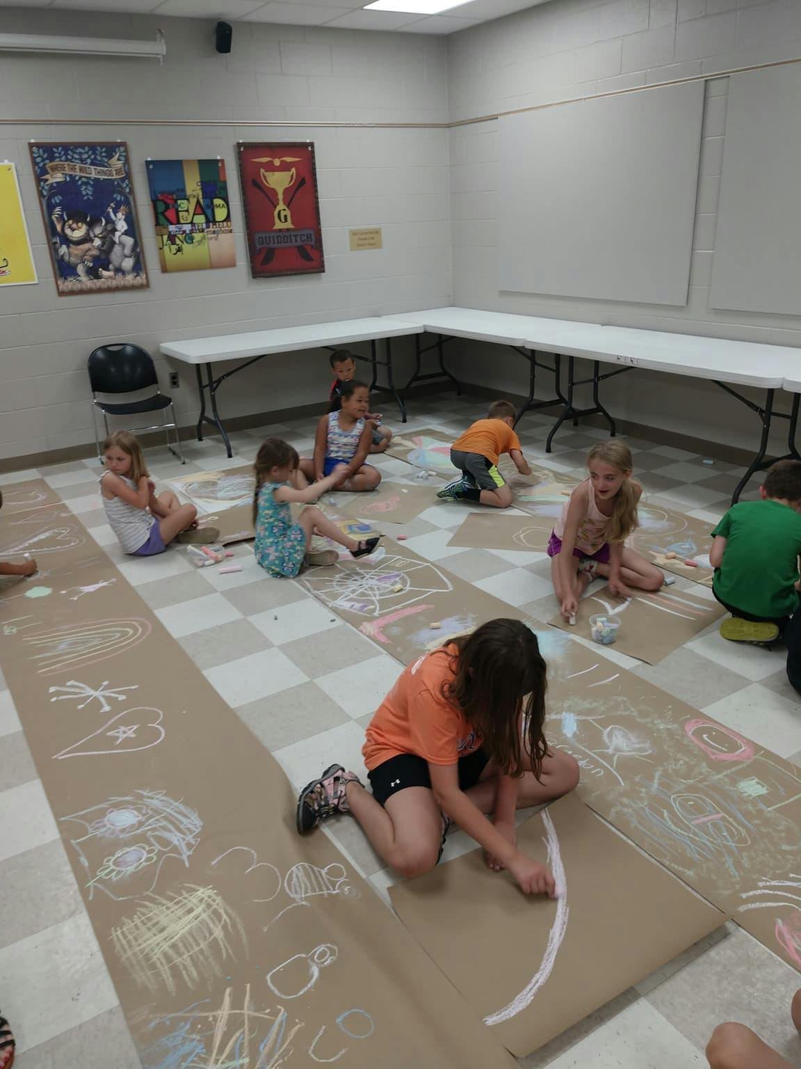 Children drawing with chalk on paper on the floor
