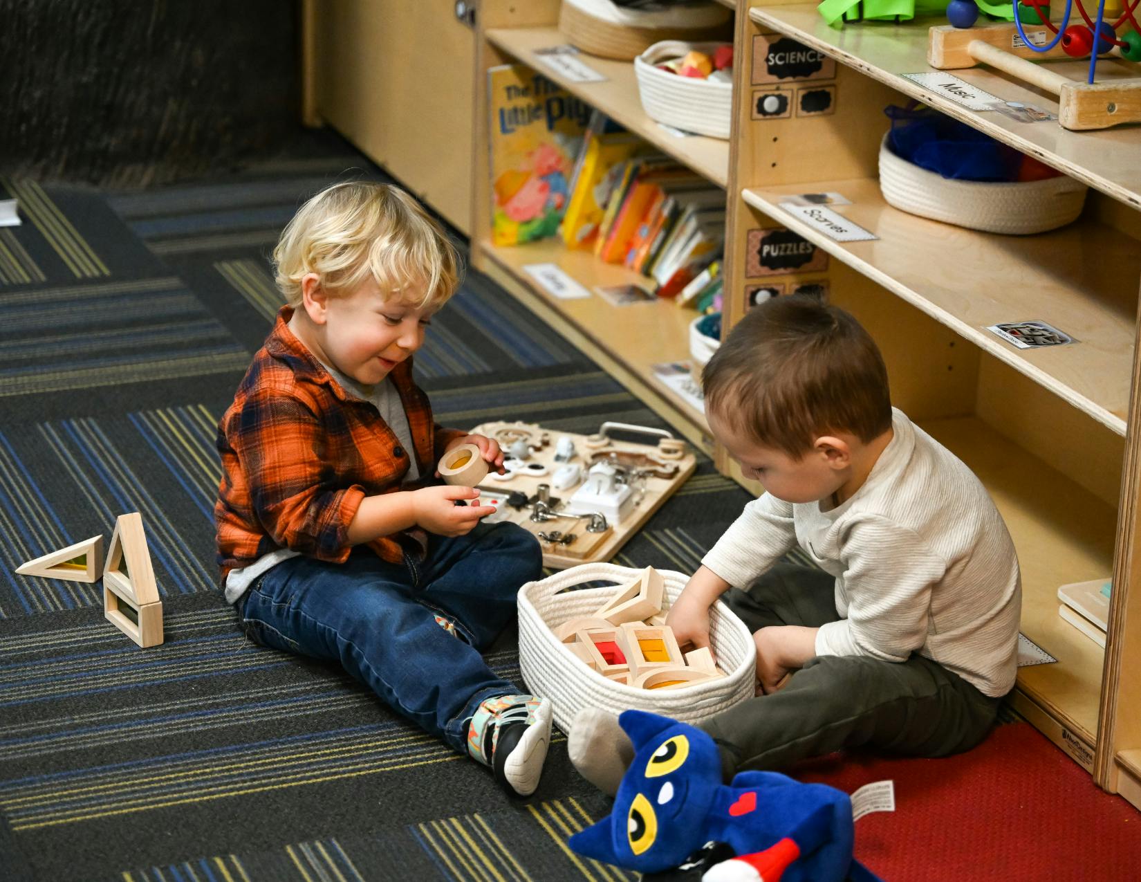 Two children playing with toys on the floor in a classroom