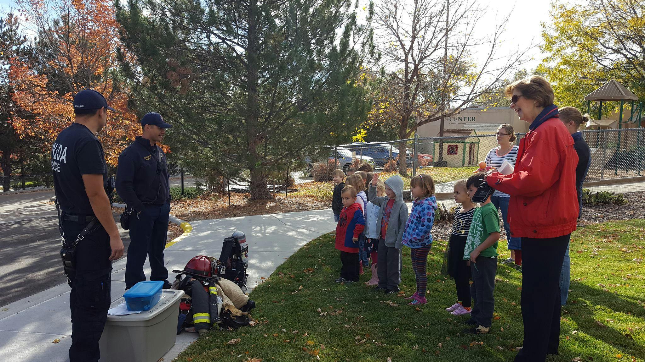 Two people in uniform talking to a group of children and adults outdoors