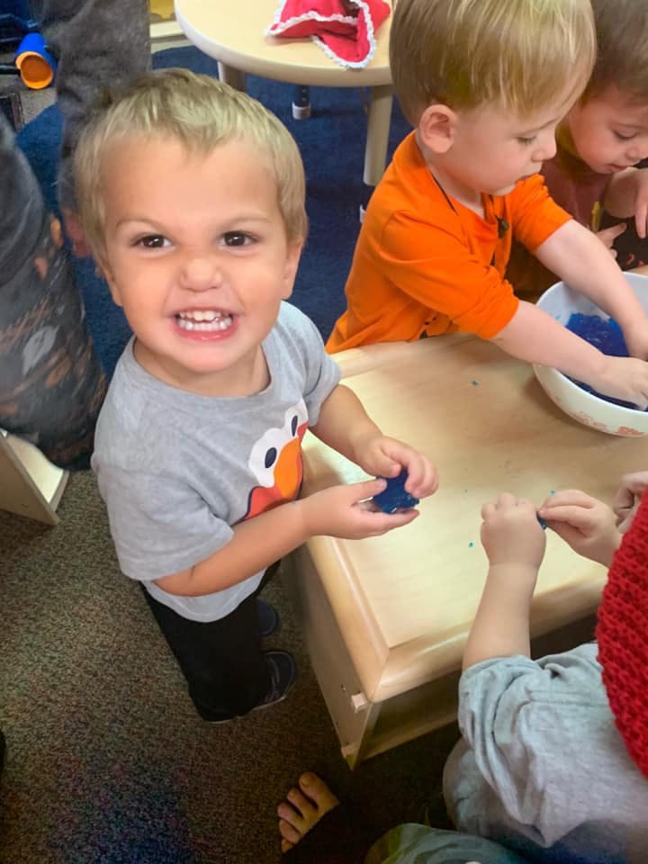 Child holding blue playdough, another child playing with blue material in a bowl