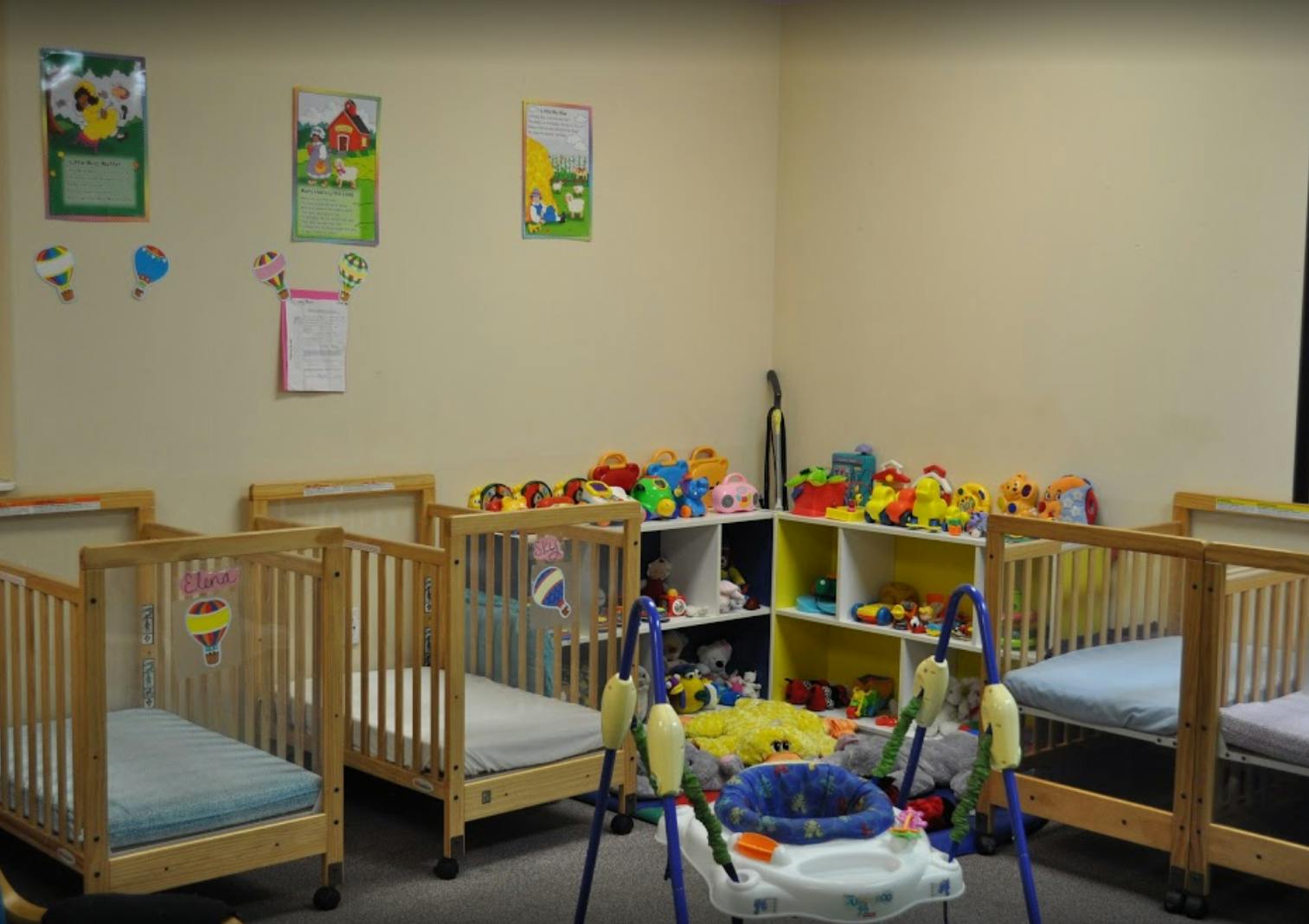 Multiple cribs in a room with shelves of toys and baby equipment