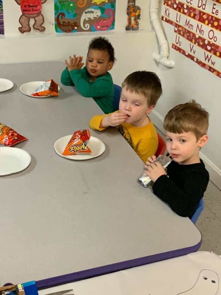 Three children sitting at a table with snacks