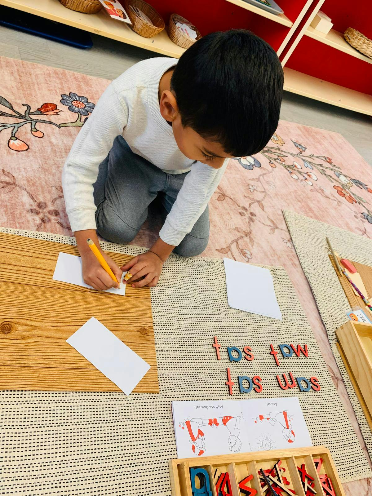 Child writing on paper with a pencil in a classroom setting