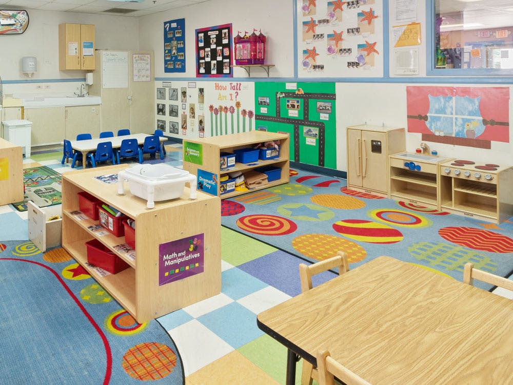 Colorful preschool classroom with tables, chairs, shelving units, and play kitchen area