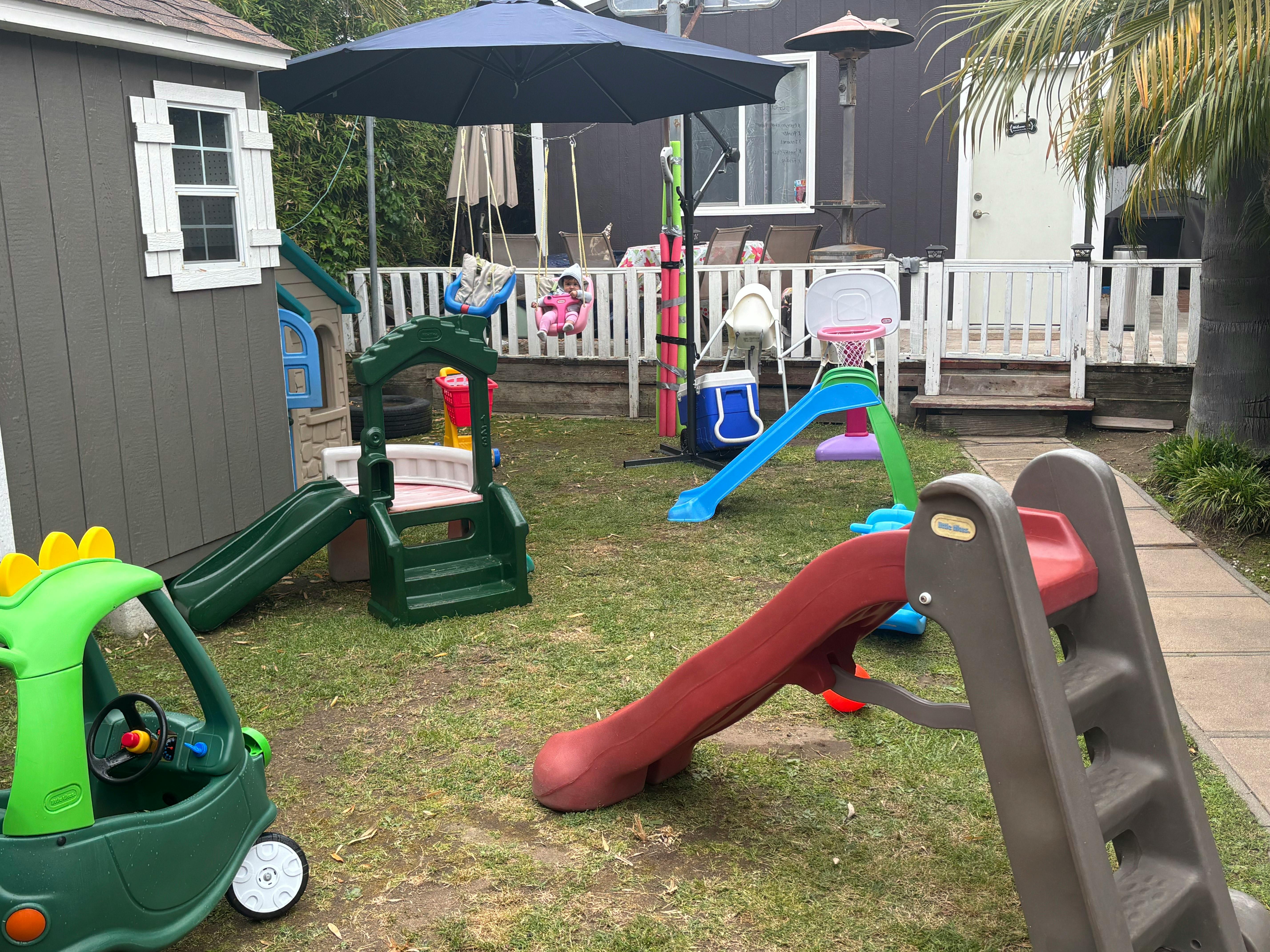 Child in a swing in a backyard filled with various plastic play equipment