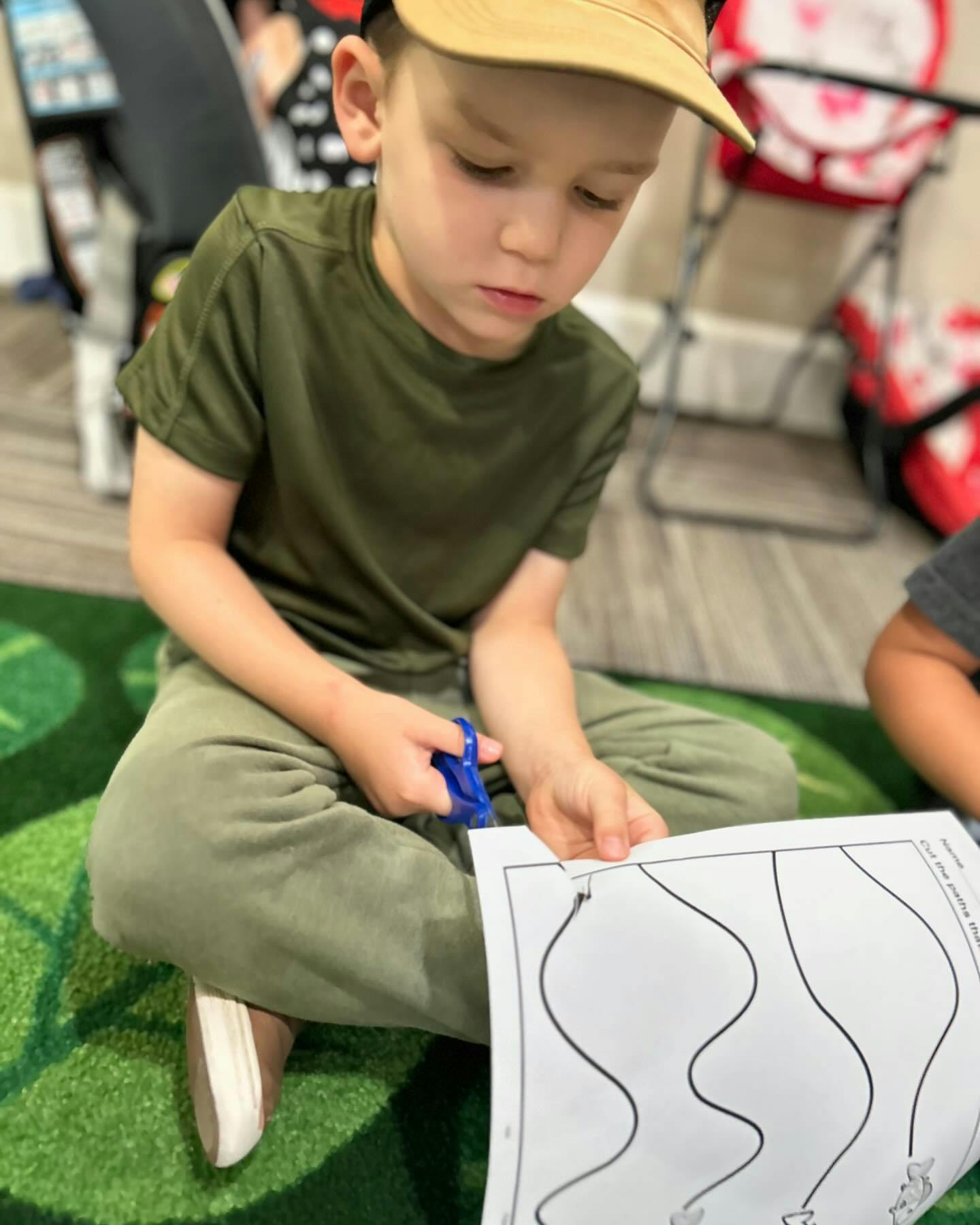 Child sitting on a rug and using scissors to cut a paper worksheet
