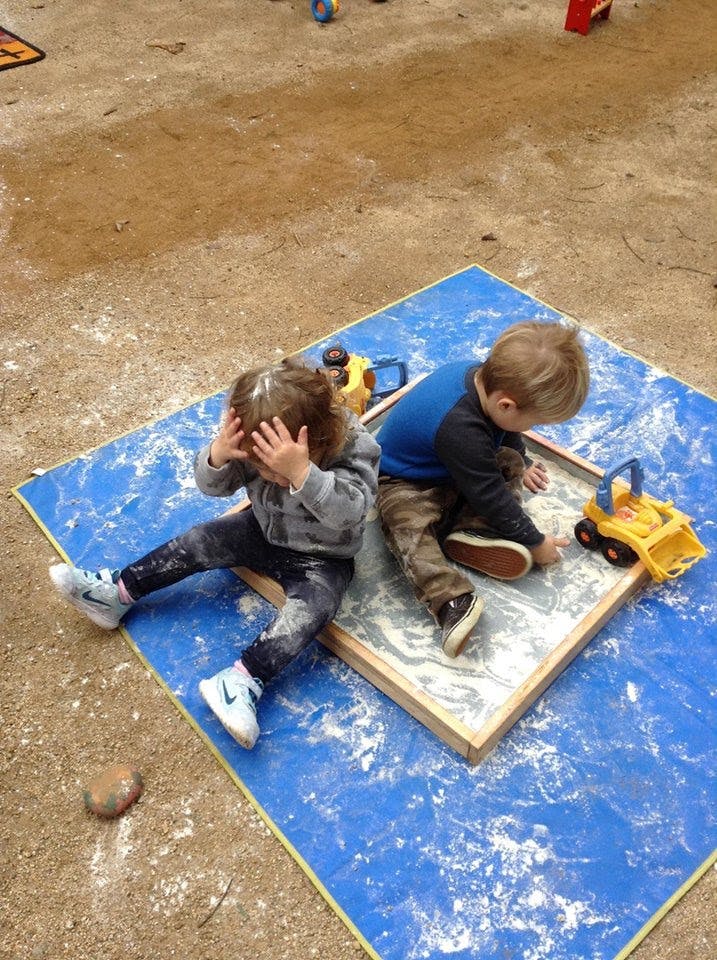 Two children playing in a sandbox with toys