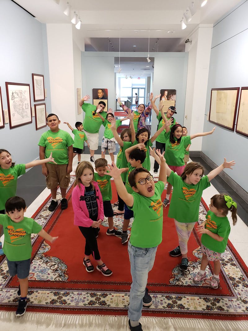 Group of children and adults in green shirts posing with arms raised in a hallway