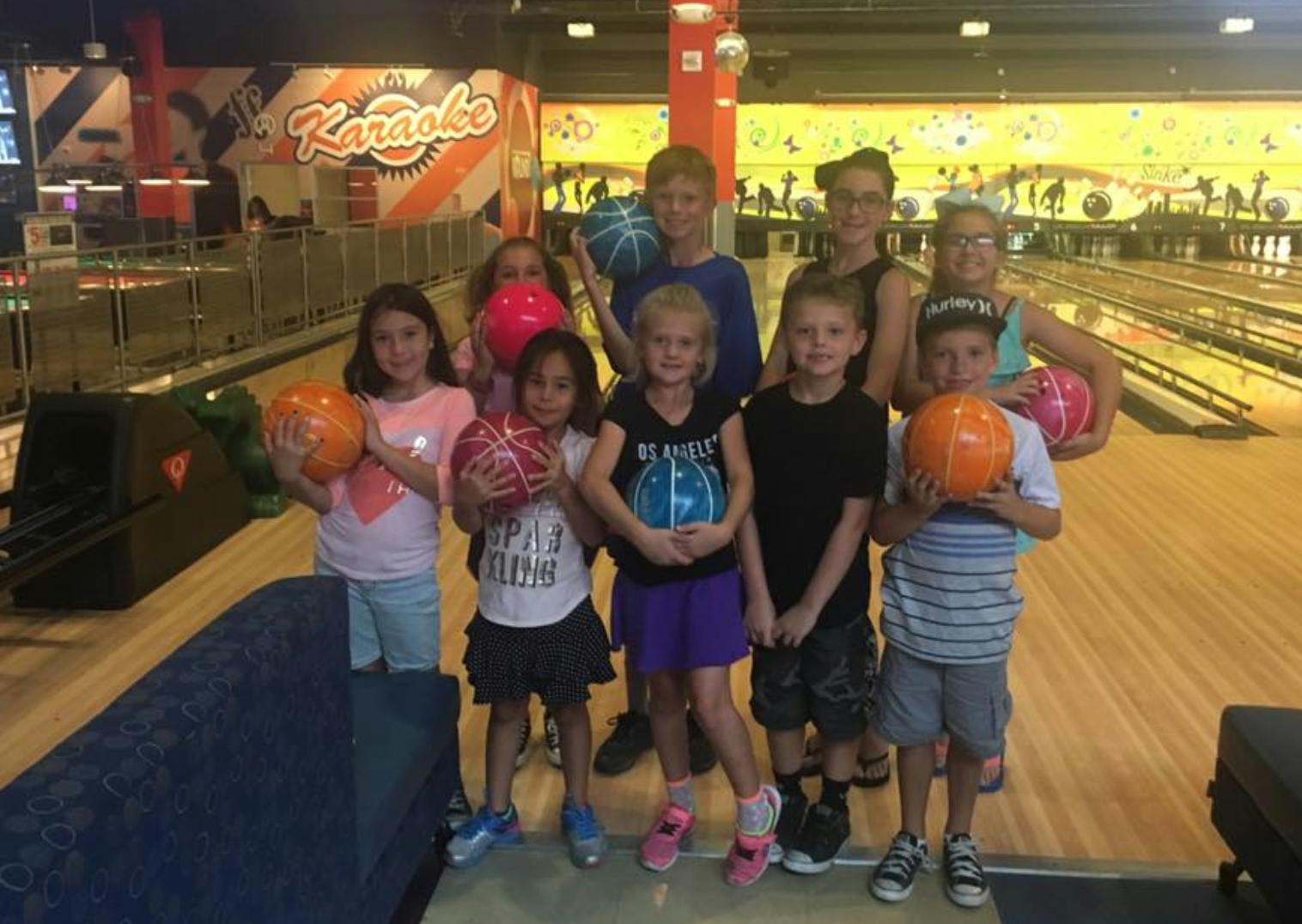 Group of children and teens holding bowling balls in a bowling alley