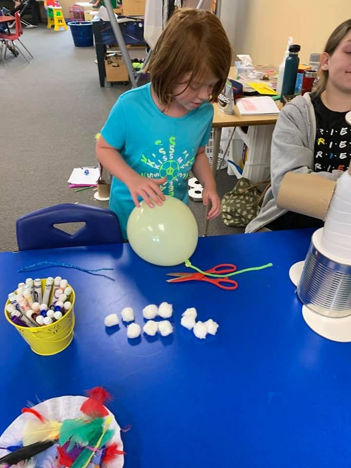 Child working on a craft project with a balloon and cotton balls