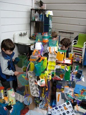 Two children playing with a large structure made from recycled materials
