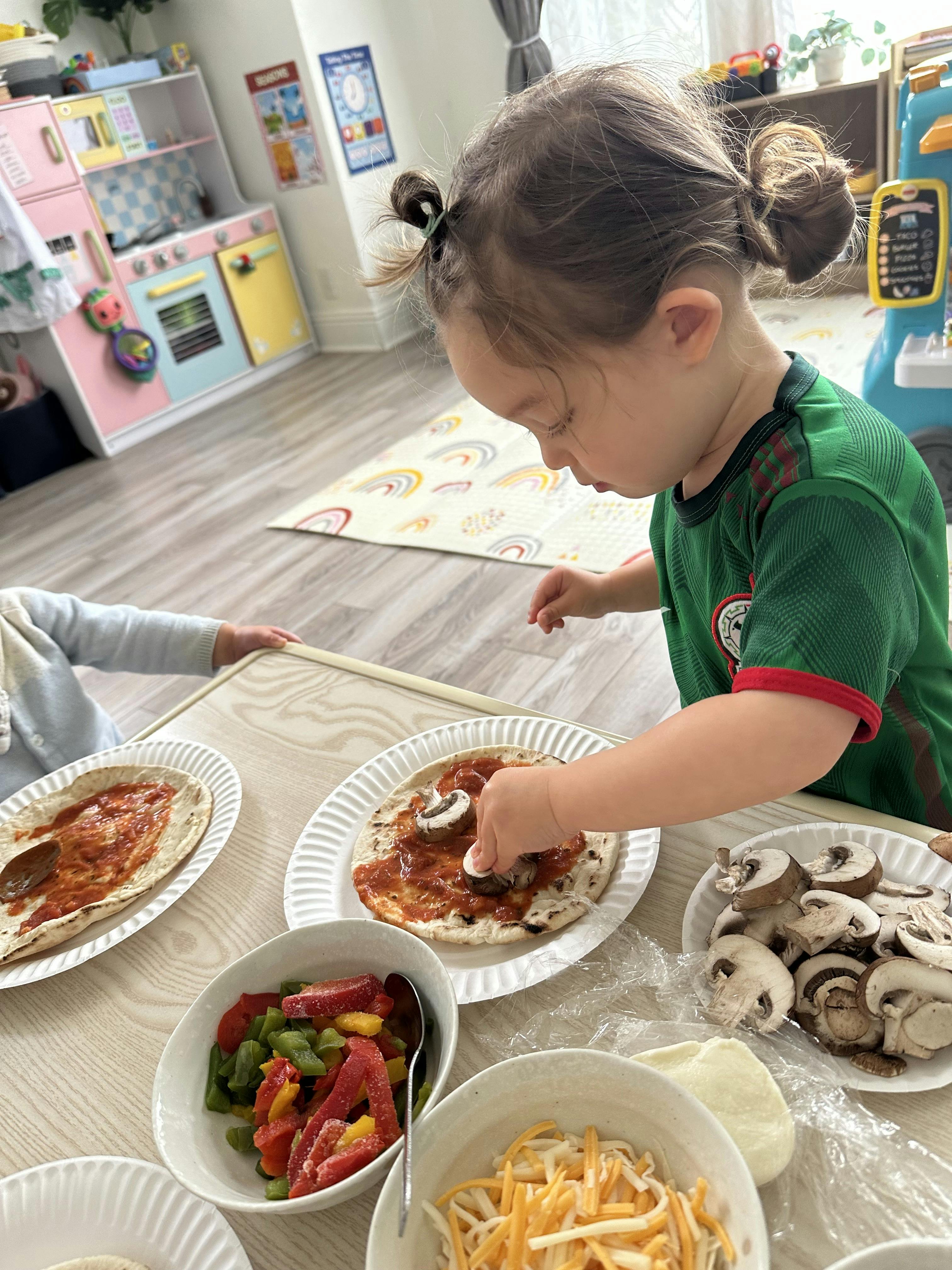 Child placing a mushroom slice onto a pita pizza base