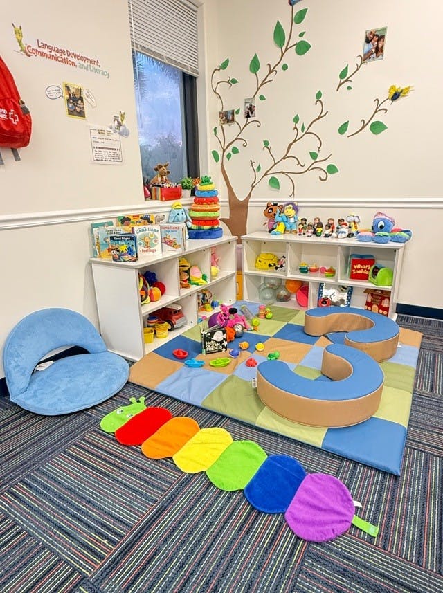 Child's play area with shelves of toys, books, floor mat, and cushion seating