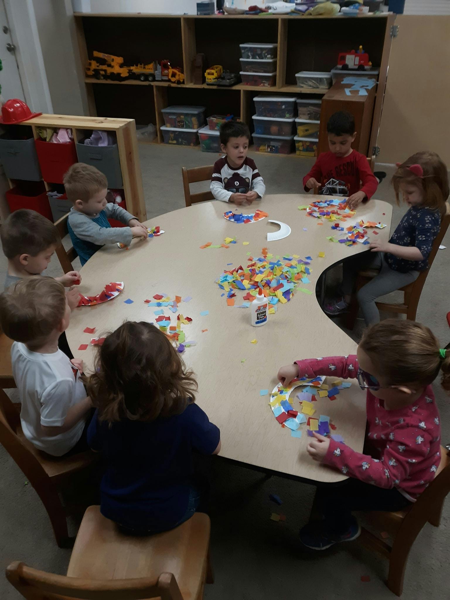 Children sitting around a table doing crafts with colorful craft supplies