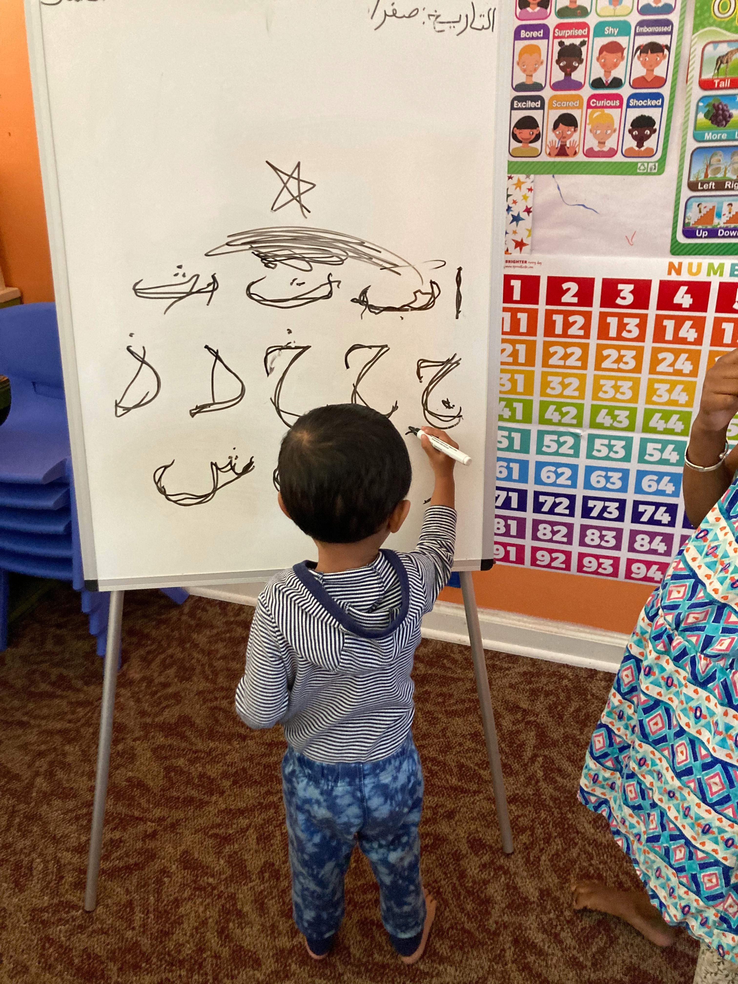 Child drawing Arabic letters on a whiteboard with a marker
