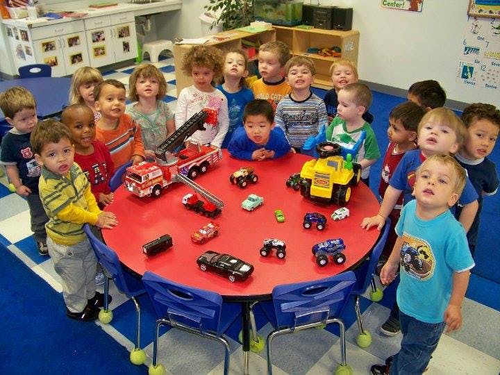 Children gathered around a red table with toy vehicles