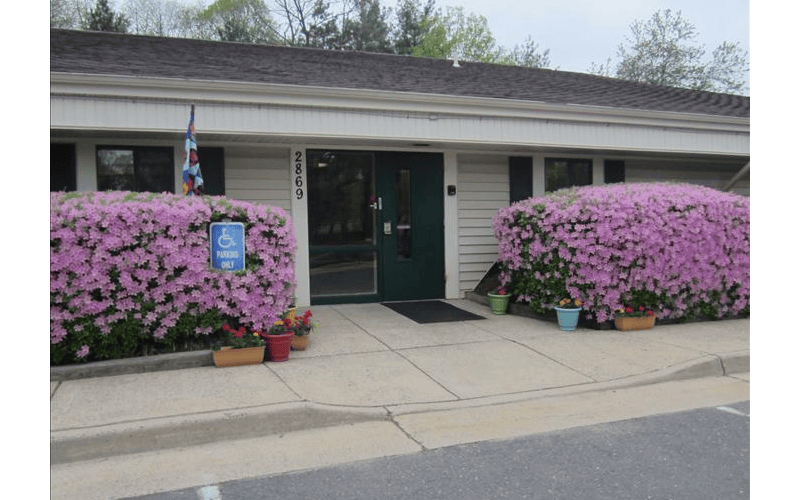 Entrance to a building with pink blooming bushes and a handicap parking sign