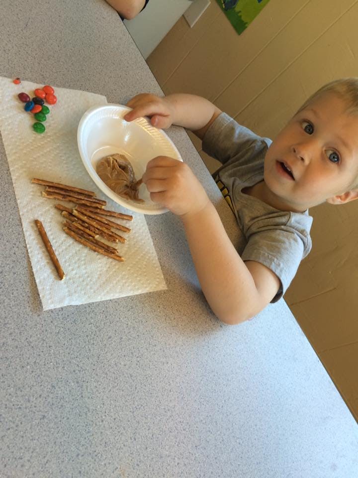 Child holding a bowl of peanut butter with pretzels and candies on a napkin