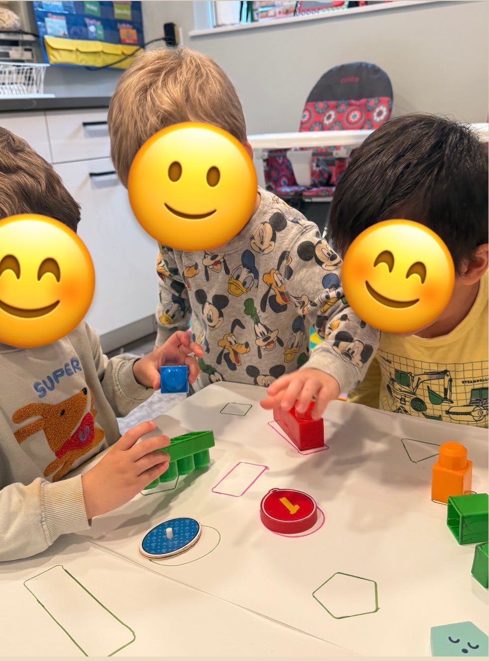 Three children playing with blocks and shape sorters on a white table