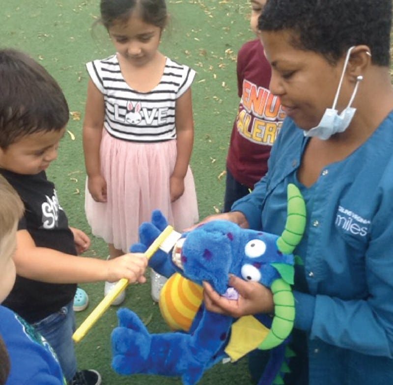 Adult and children brushing teeth on a blue stuffed animal