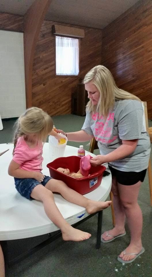 Person and child bathing a doll in a red basin