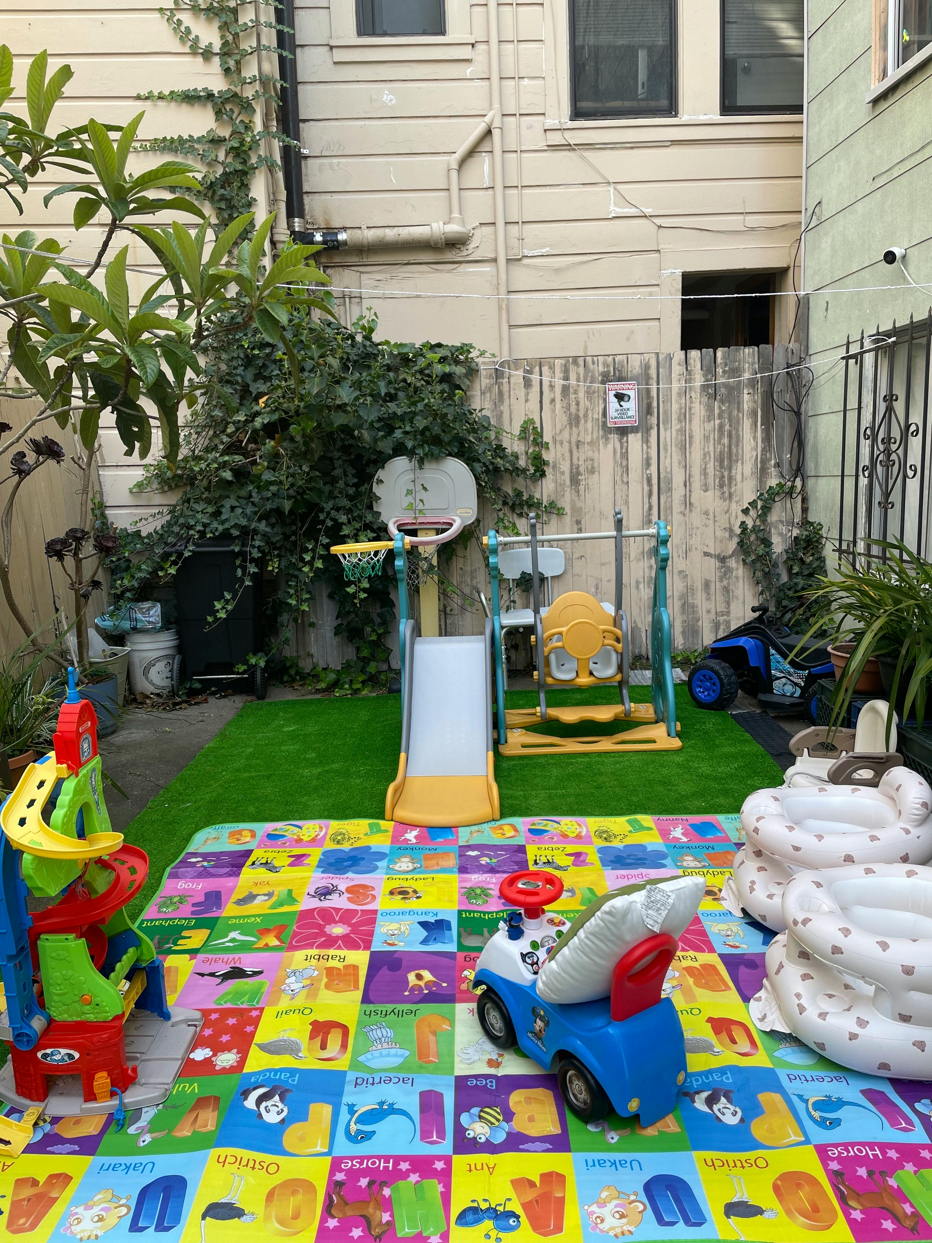backyard play area with a colorful alphabet mat, plastic slide, and ride-on toys