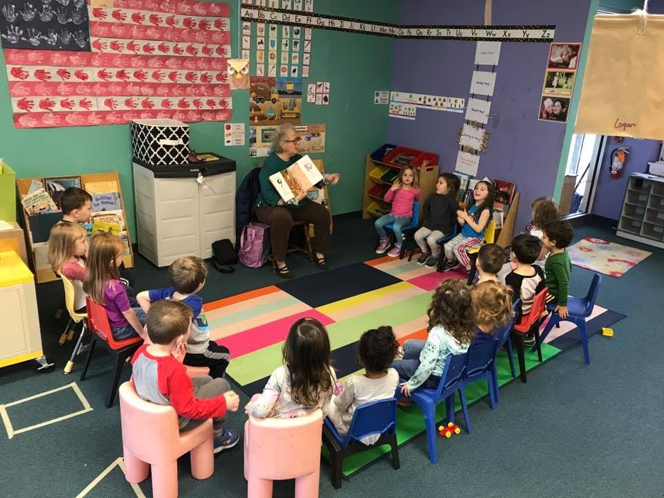 Adult reading a book to a group of children in a classroom