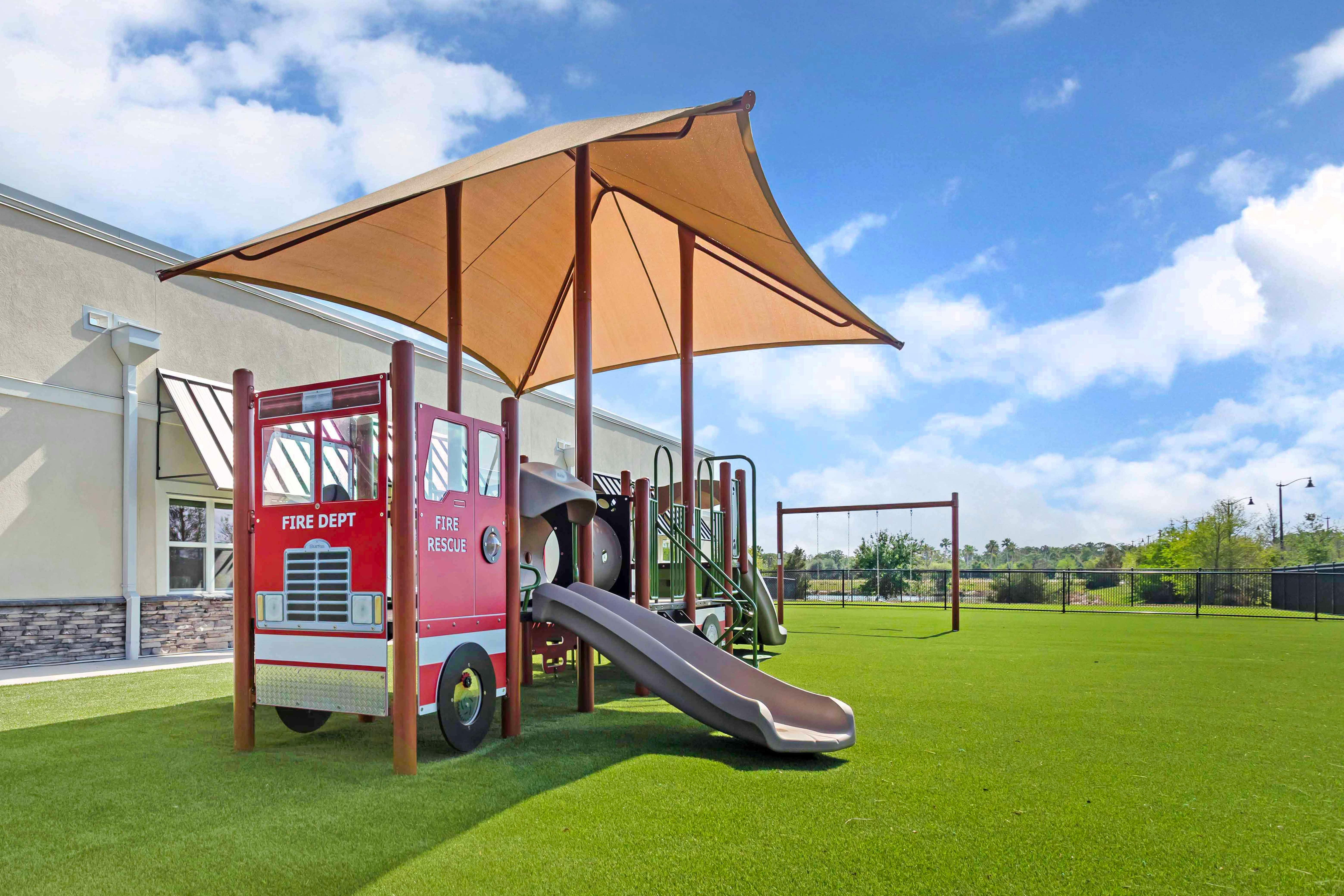 Playground with a red fire truck structure and a slide on artificial grass