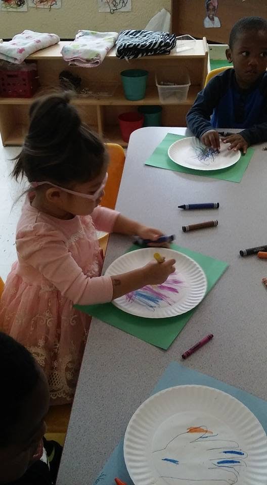 Child coloring on a paper plate at a table in a classroom