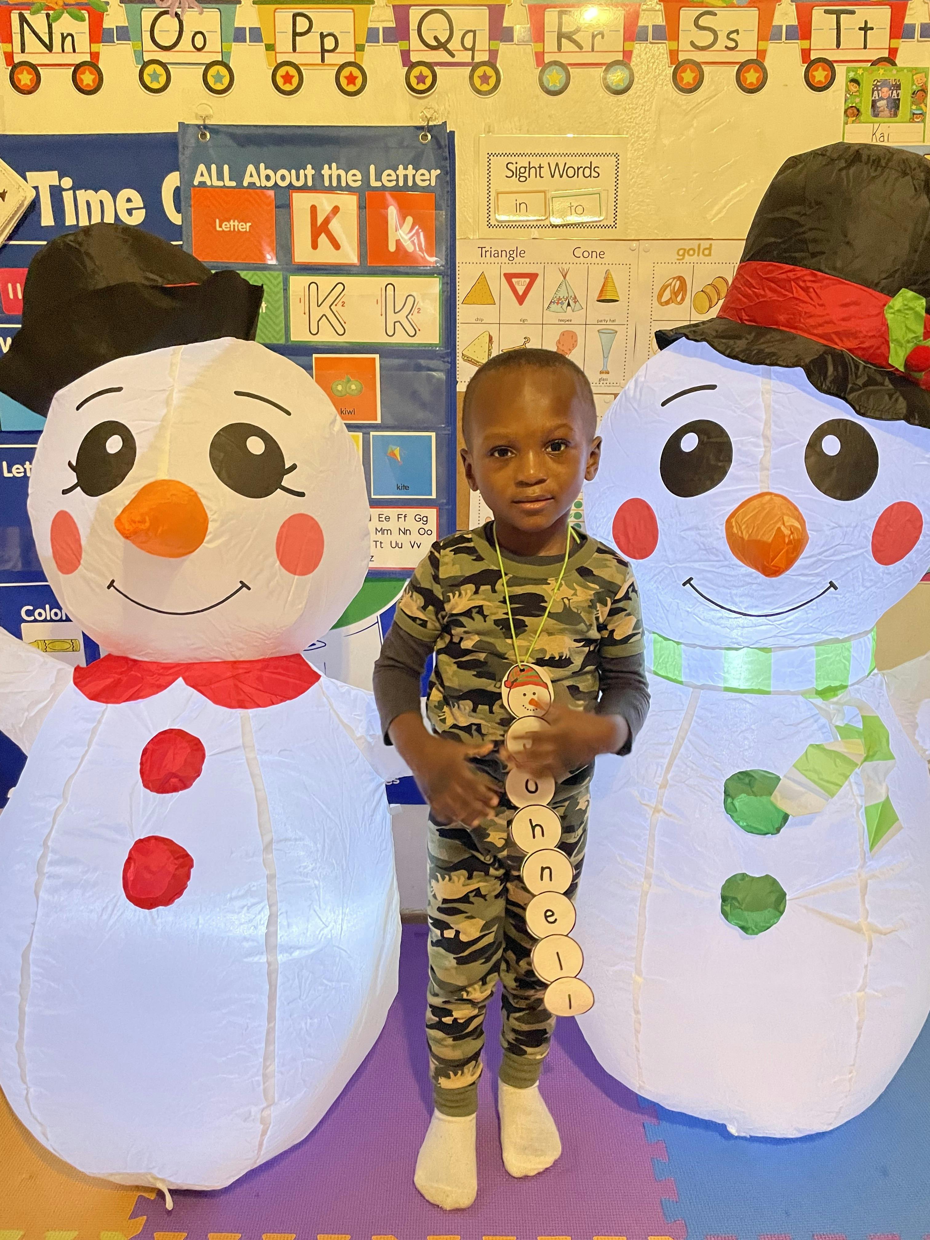 Child in camouflage pajamas standing between two inflatable snowmen