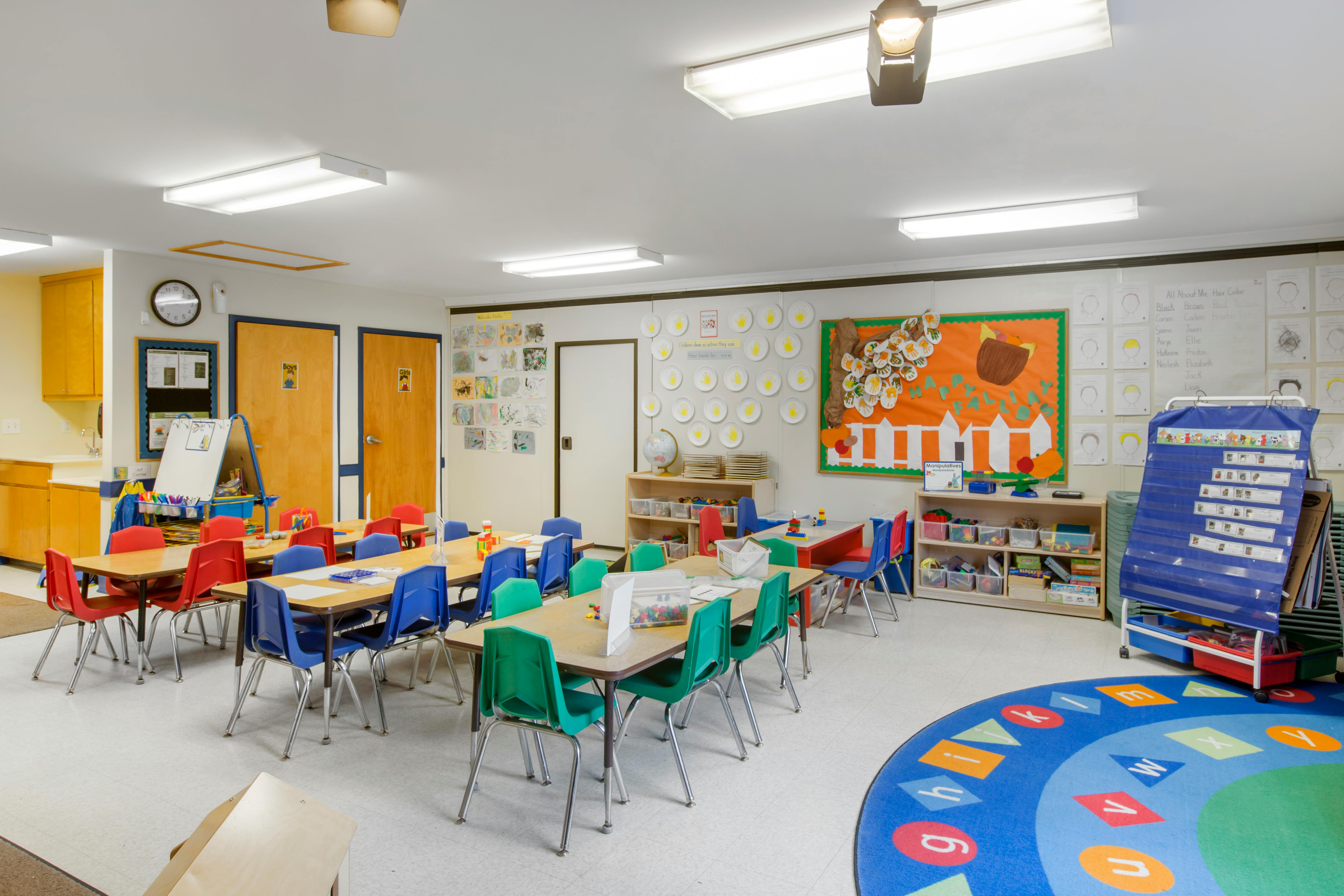 An empty classroom with small tables and chairs, a sink, and wall decorations