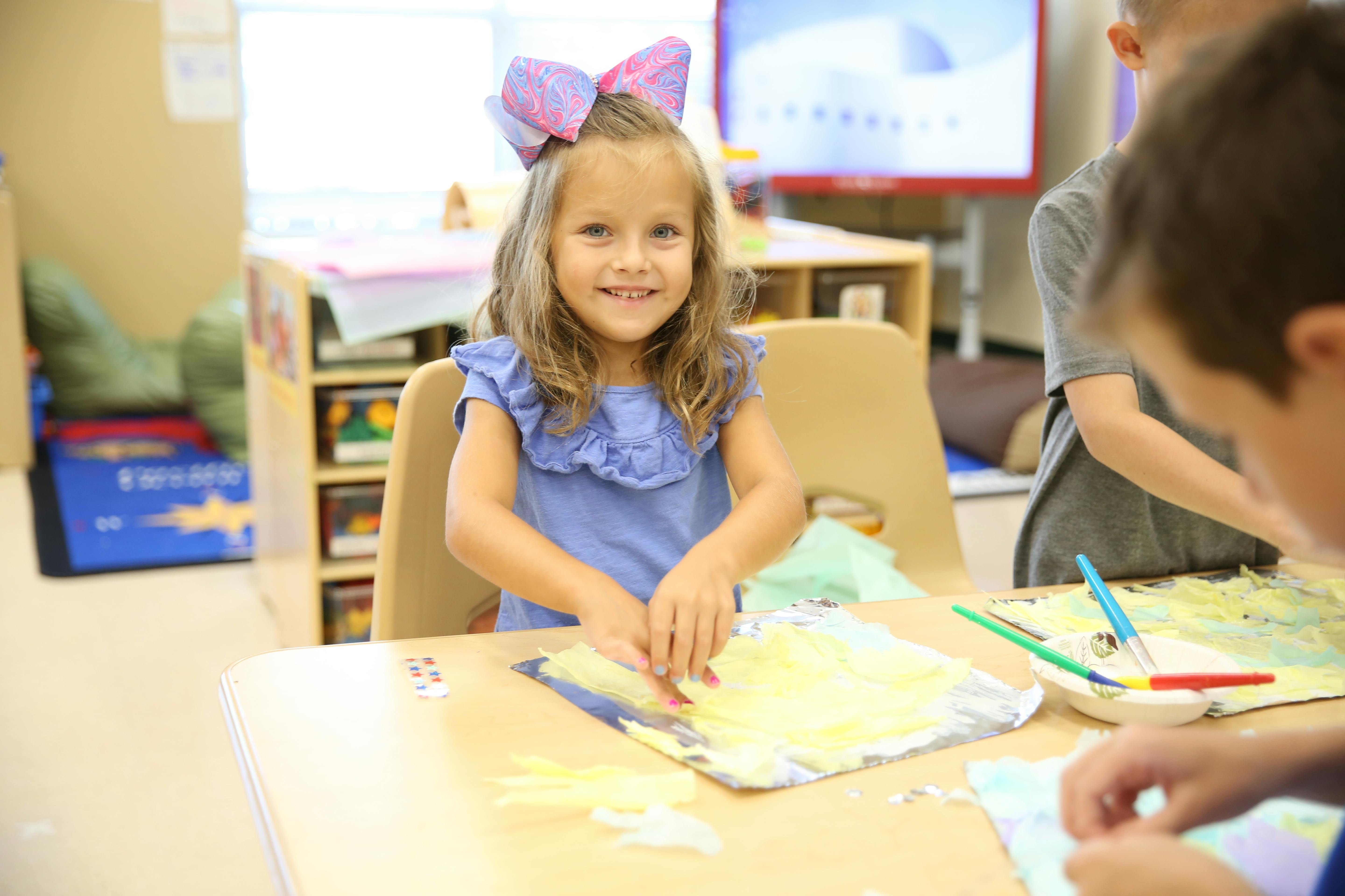 Child with bow on head doing an art project at a table